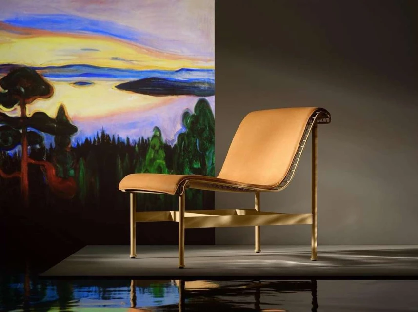 Tan leather chair with gold frame in front of a landscape painting backdrop, set on a dark grey reflective surface.