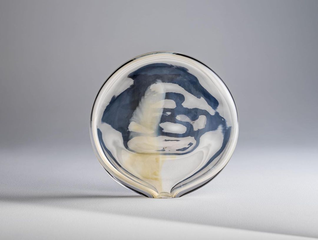 Close-up studio shot of a clear glass bowl with an abstract blue and white design inside, on a seamless neutral gray background.