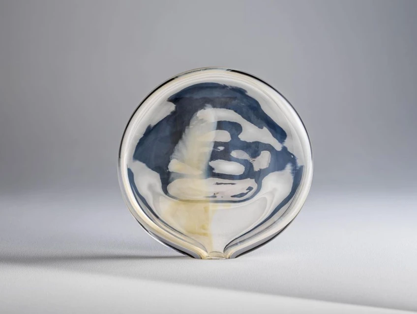 Close-up studio shot of a clear glass bowl with an abstract blue and white design inside, on a seamless neutral gray background.