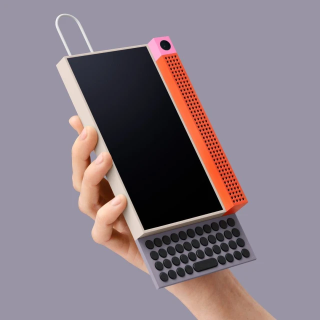Hand holds a stylized retro-inspired device with a screen, speaker, and keyboard, presented against a clean, solid-color backdrop.