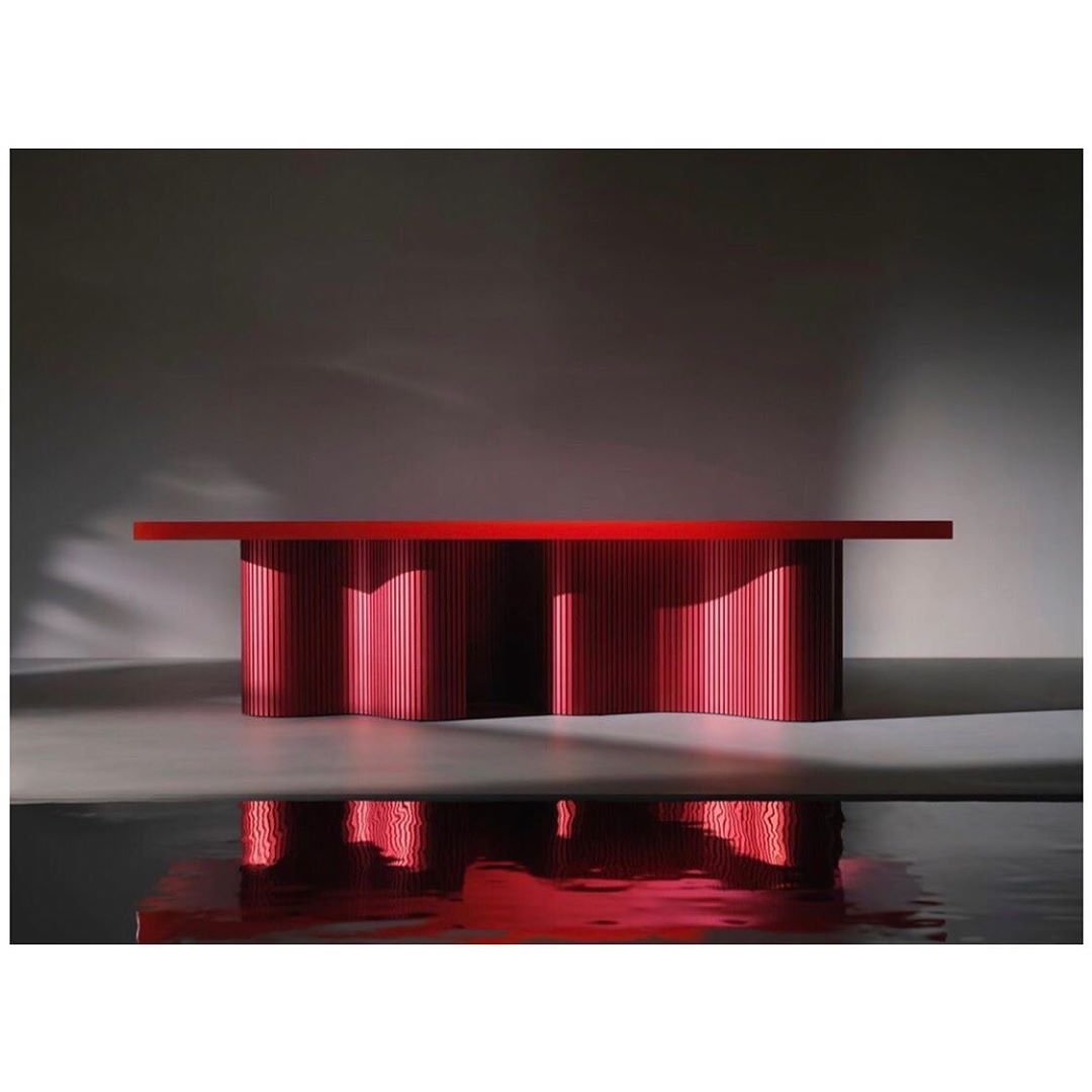 Eye-level shot of a modern red table with vertical slats in a minimalistic studio setting. Reflections are visible on the floor.