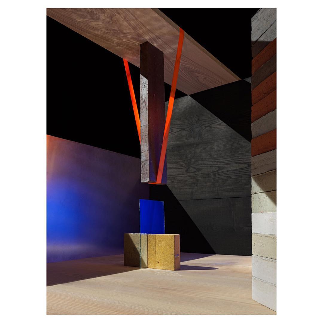 Abstract geometric installation with cinder blocks, wood planks, and colored lighting casting shadows in a minimalist interior space.