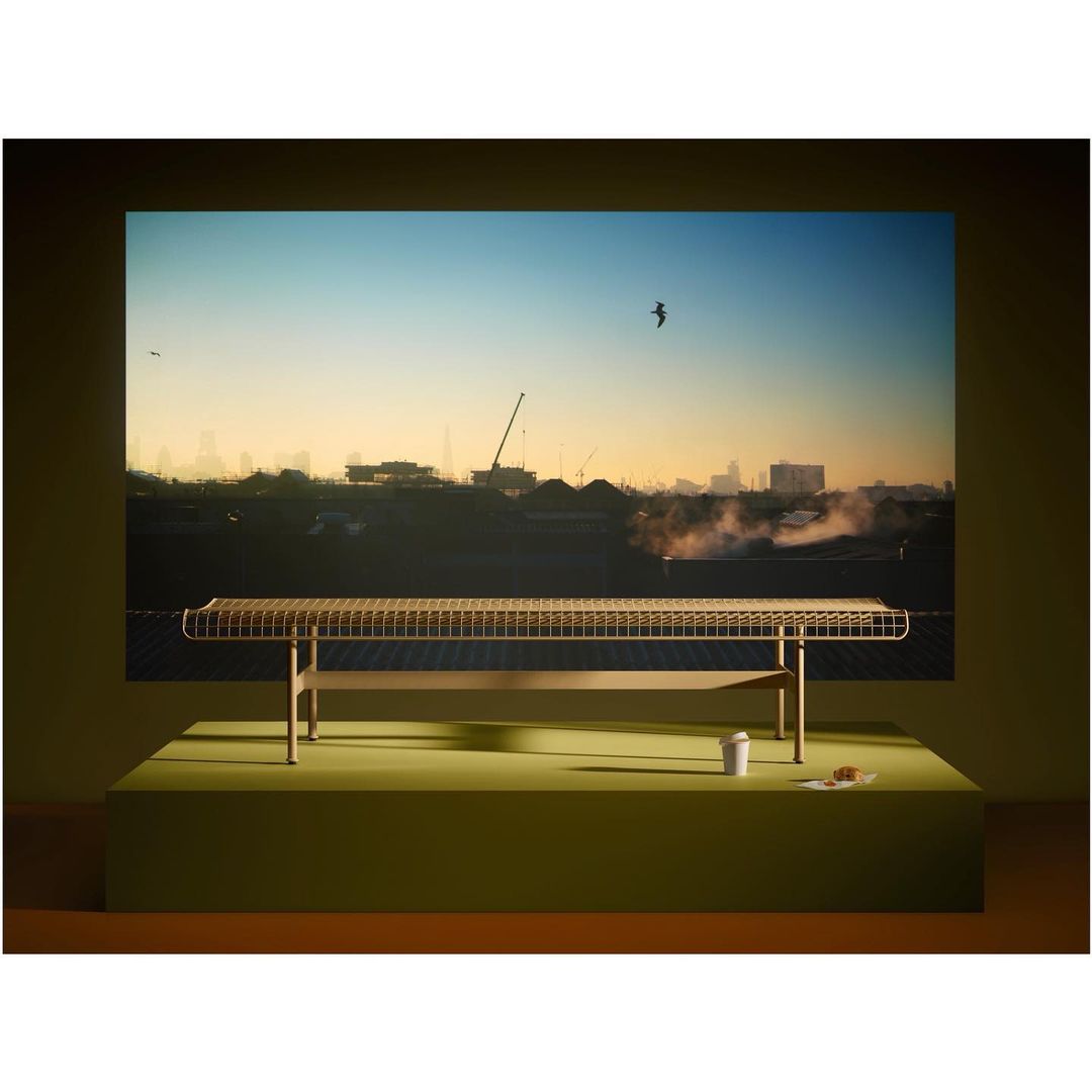 Woven bench on a lime green platform in a studio, displayed against an image of a cityscape during sunrise.