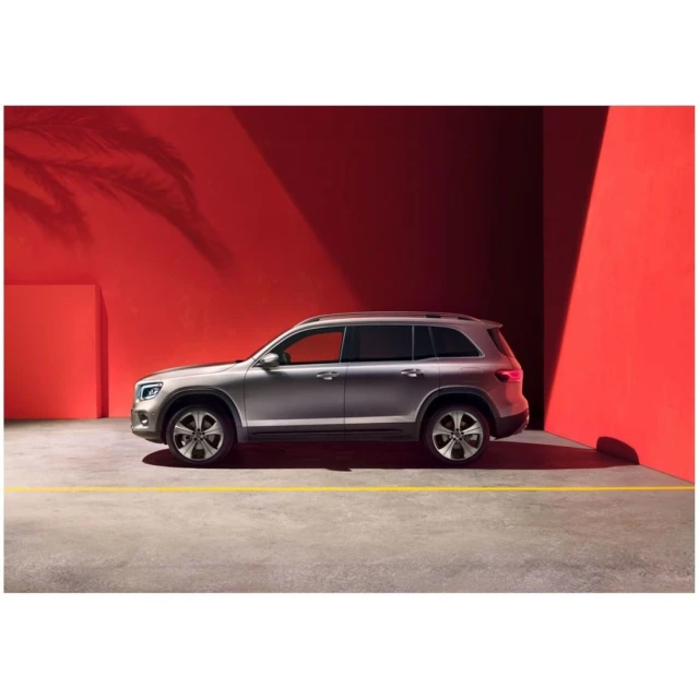 Silver SUV parked indoors against a red wall with shadow of a plant, showcasing automotive design and modern industrial environment.