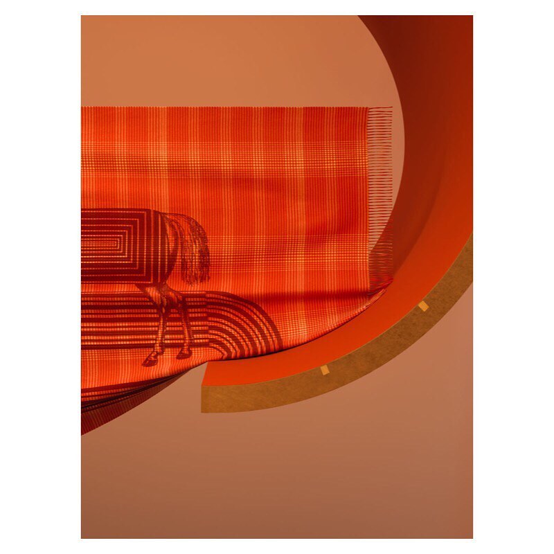Still life shot of an orange plaid blanket with a horse graphic, draped over a curved orange and brown structure against a solid background.