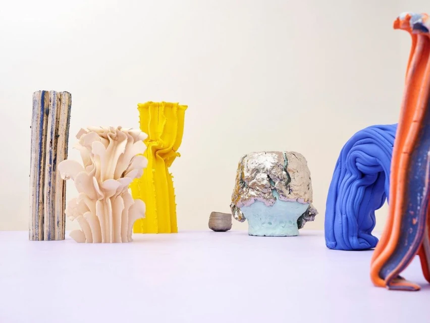 Abstract arrangement of colourful ceramic objects in front of a white background in a studio setting. The colours present are yellow, blue and silver.