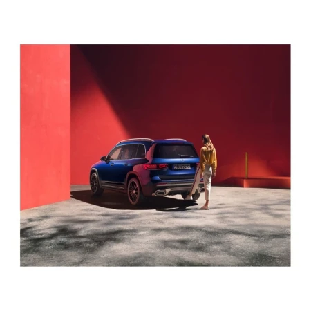 Blue SUV parked against a bright red architectural wall with a woman standing beside it in a courtyard.