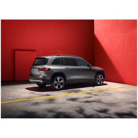 Gray Mercedes-Benz GLB SUV parked indoors against a vivid red wall with a yellow line marking the parking space. Automotive photography.