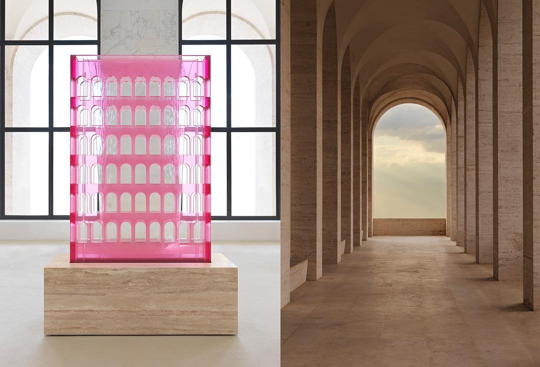 Pink architectural model on a beige base in front of window and travertine colonnade architectural background.