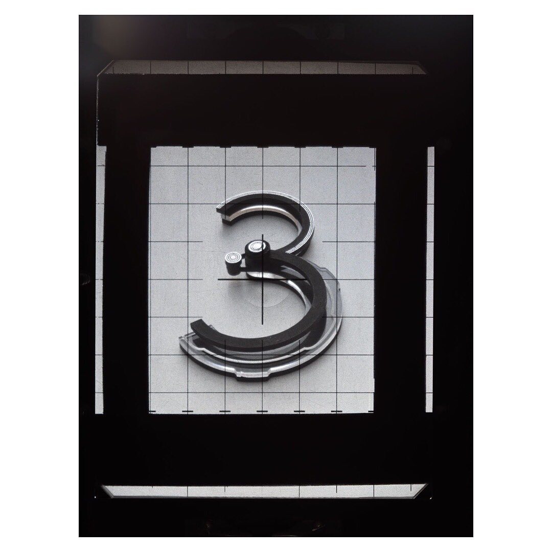 Abstract shot of the number three centered, made of layered grey material, surrounded by dark-grey square frame and a light-grey grid