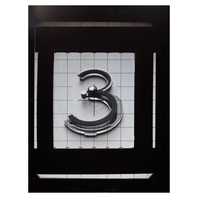 Abstract shot of the number three centered, made of layered grey material, surrounded by dark-grey square frame and a light-grey grid