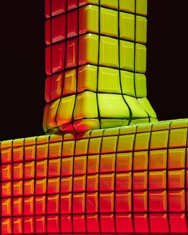 Abstract shot of interconnected yellow and red cube-like structures against a dark background creating a visually distorted, grid-like pattern.