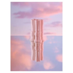 A sculptural pink ceramic pillar object centered on a reflective surface against a soft pink sunset sky background.