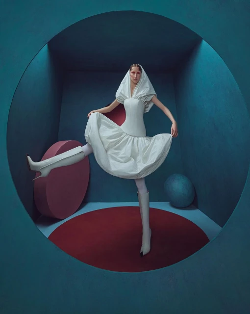 Woman in a couture white dress and matching hood poses inside a circular blue doorway with red and blue geometric shapes.
