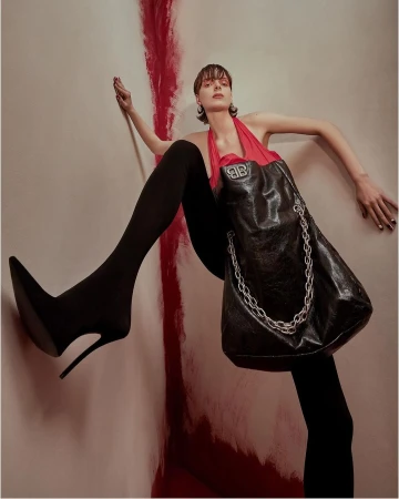 Fashion shot: a woman in black tights and heels, posing with a designer bag, against a painted wall with shades of red and beige.