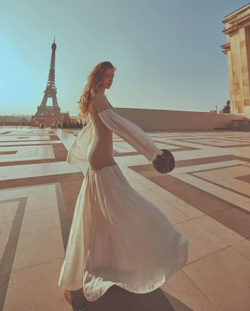 A woman in a flowing dress poses in front of the Eiffel Tower on a sunny day, capturing the essence of fashion and Parisian elegance.