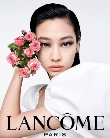 Elegant Asian woman with smoky eyeshadow holds pink roses in a beauty campaign for Lancôme, against a stark white background.