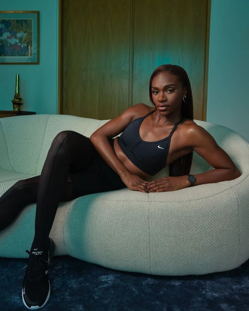 Athletic woman in sports bra and leggings lounges on an off-white couch, wearing black sneakers. Indoor setting, fitness and fashion.