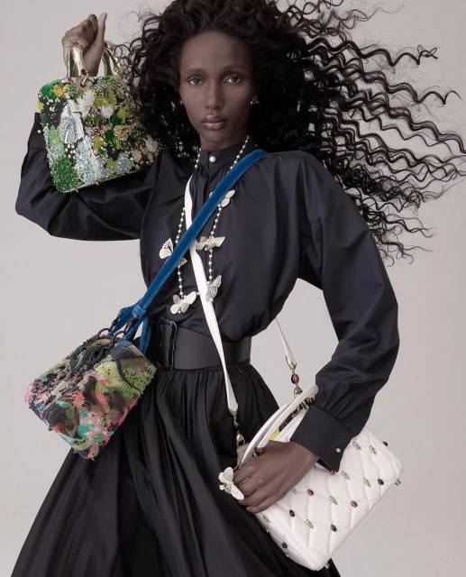 Fashion shot featuring a dark-skinned woman in a black dress, holding and wearing multiple colorful, decorative purses in a studio.