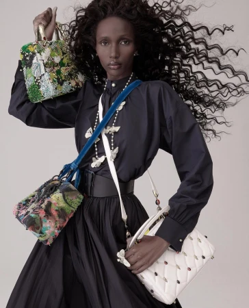 Fashion shot featuring a dark-skinned woman in a black dress, holding and wearing multiple colorful, decorative purses in a studio.
