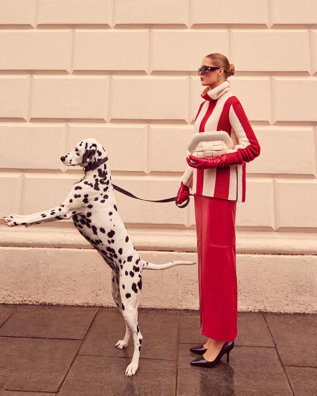 Woman in red and white striped sweater and red skirt poses with a dalmatian dog on a city sidewalk.