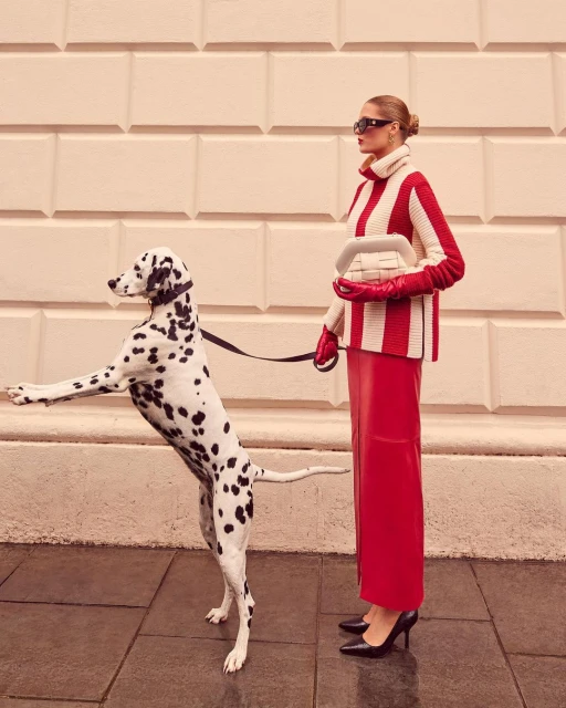 Woman in red and white striped sweater and red skirt poses with a dalmatian dog on a city sidewalk.