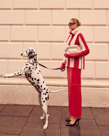 Woman in red and white striped sweater and red skirt poses with a dalmatian dog on a city sidewalk.