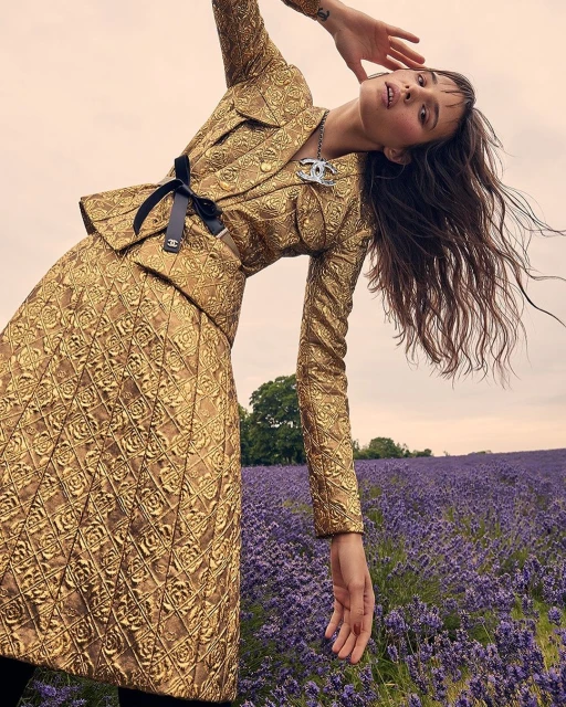 Brunette woman in gold floral Chanel skirt suit poses in a lavender field in a fashion editorial shot with natural light.