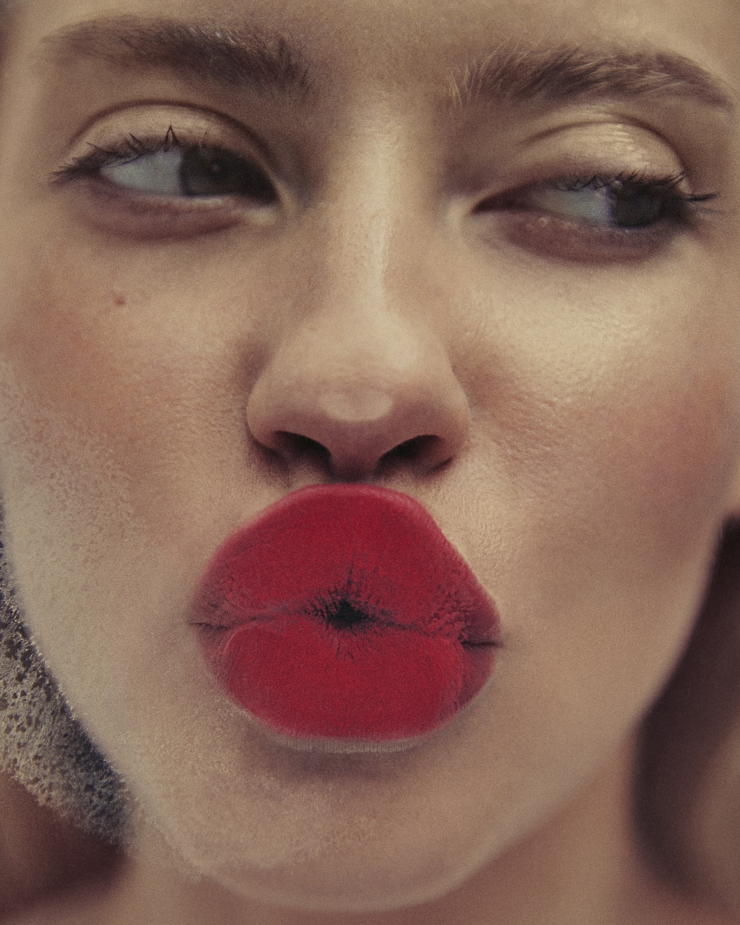 Close-up portrait of a woman with red lipstick pursing her lips and looking to the side, showcasing beauty and makeup.