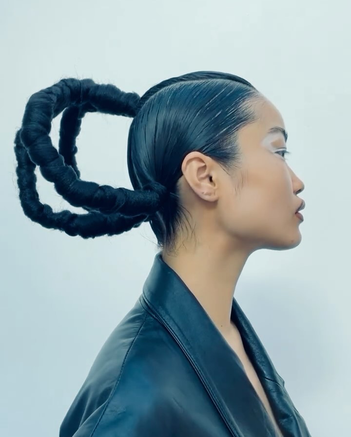 Profile shot of an Asian woman with a unique braided hairstyle, wearing a black leather jacket against a white backdrop, high-fashion aesthetic.