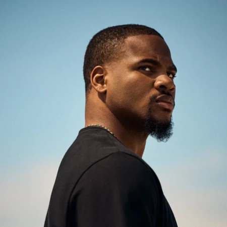 Profile portrait of a Black man wearing a black t-shirt against a clear blue sky