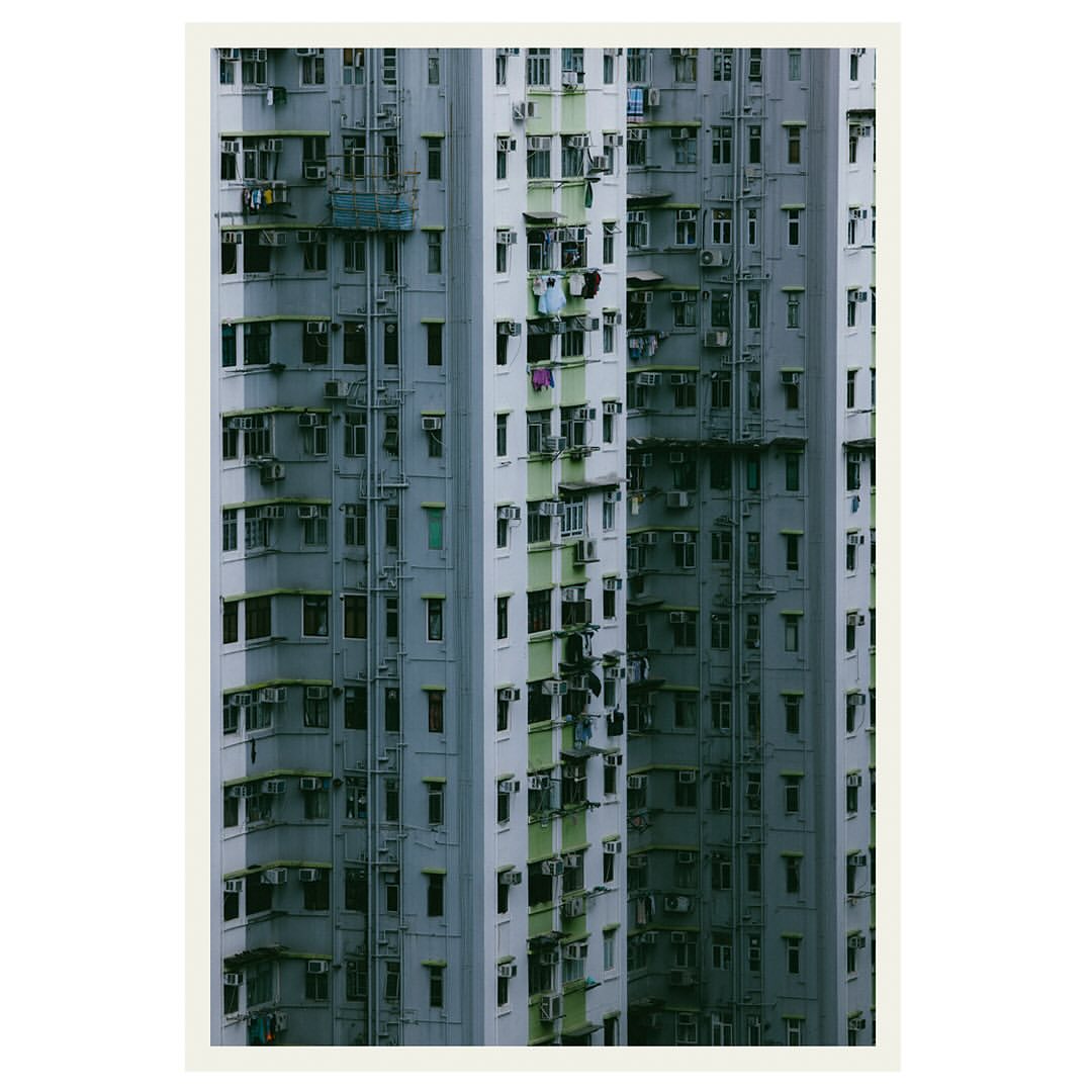 Dense urban apartment blocks tower with rows of windows and air conditioning units, emphasizing the high-density architecture of city living.