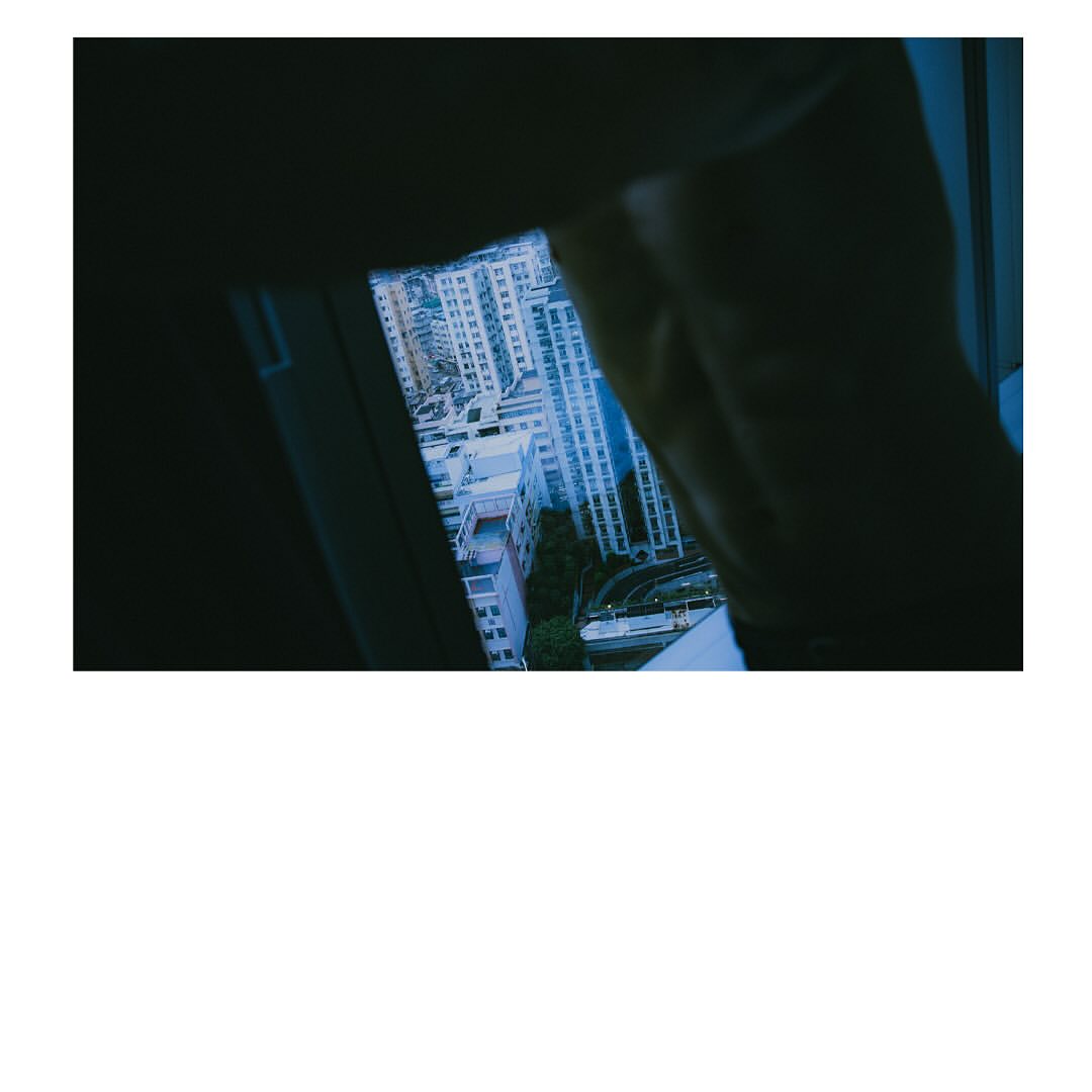 View through a window overlooking an urban scene with buildings. The sky is visible in the distance, dark tones.