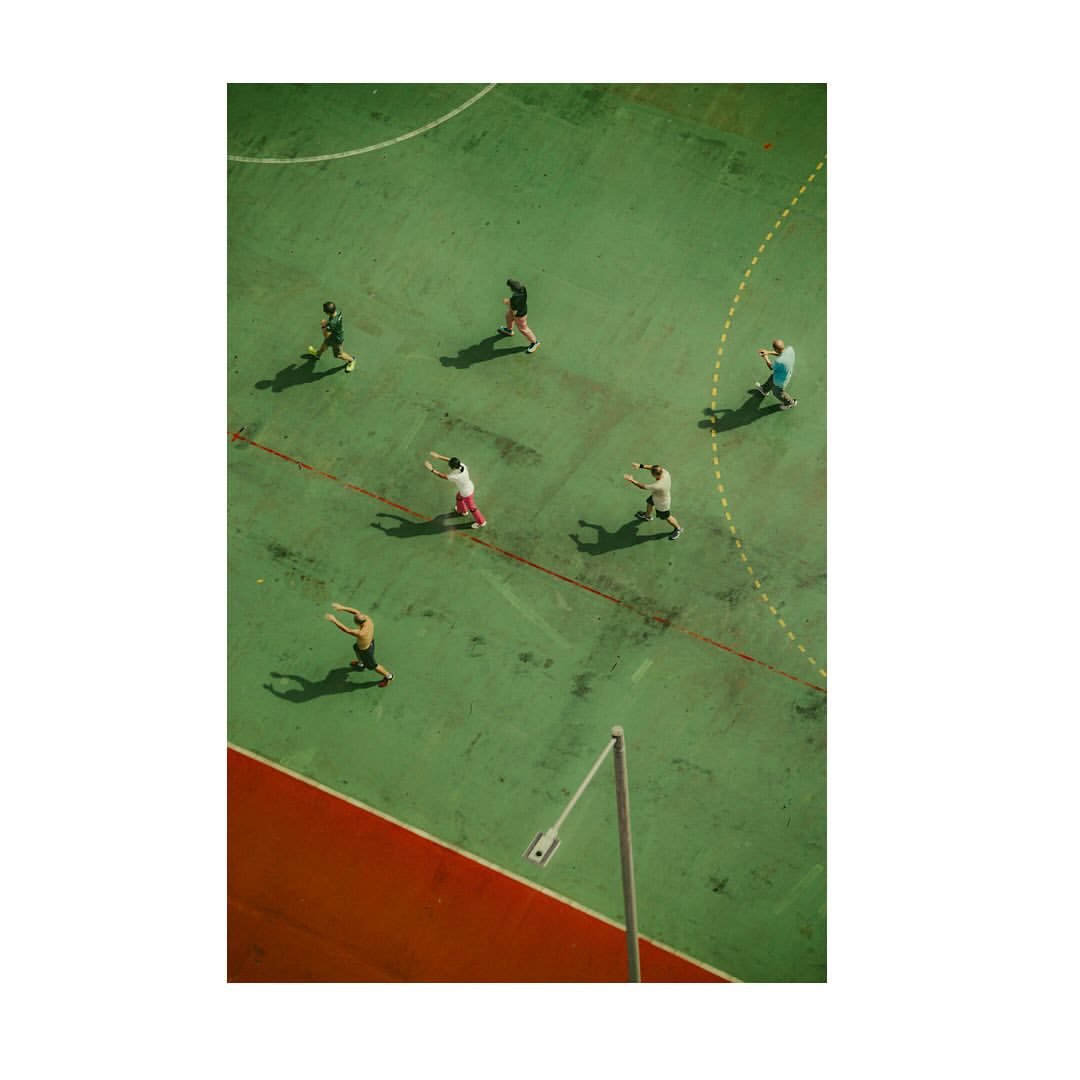 Aerial view of a group of people on an outdoor sports court with green surface and red perimeter lines, creating a dynamic and active scene.