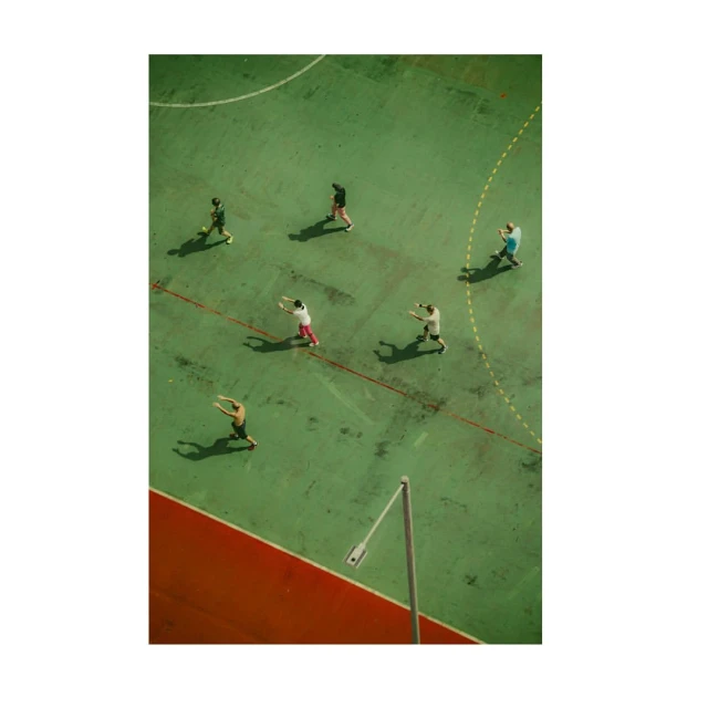 Aerial view of a group of people on an outdoor sports court with green surface and red perimeter lines, creating a dynamic and active scene.