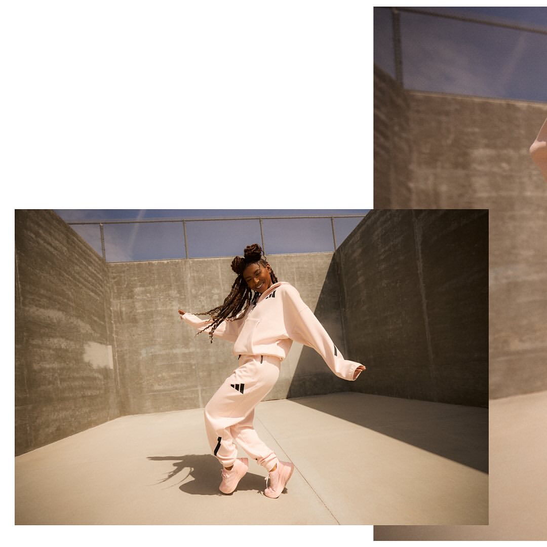 A young African American woman smiles as she dances in athletic wear with a concrete architectural background on a sunny day.