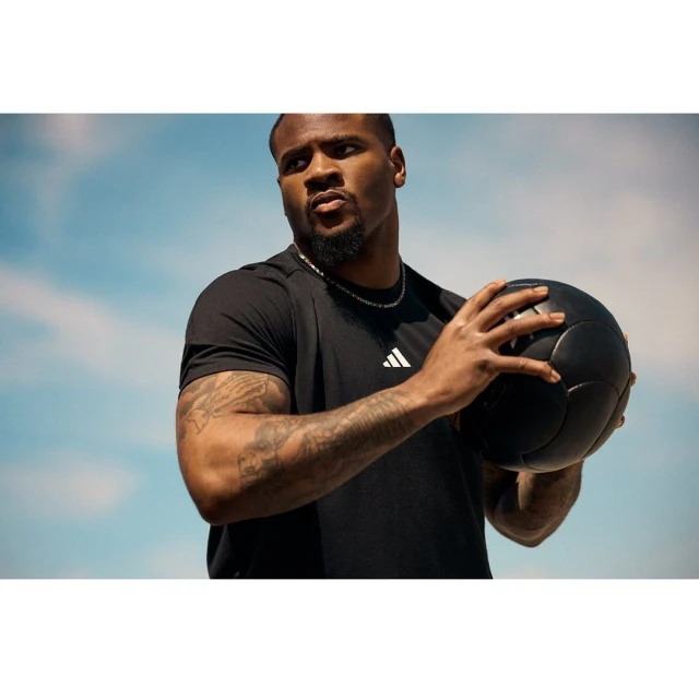 Athletic African-American man in black shirt holds black medicine ball outdoors against a sky background, fitness and exercise concept.