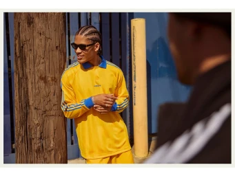Young man with braided hair wearing yellow and blue polo shirt leaning against wooden pillar outdoors
