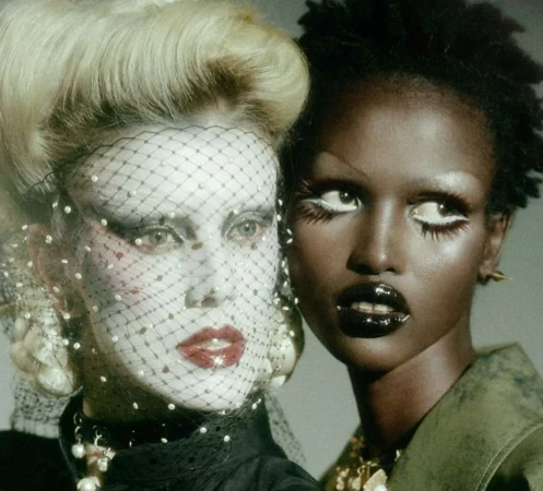 Two fashion models with dramatic makeup and hairstyles pose in a close-up studio shot, showcasing unique beauty and style.
