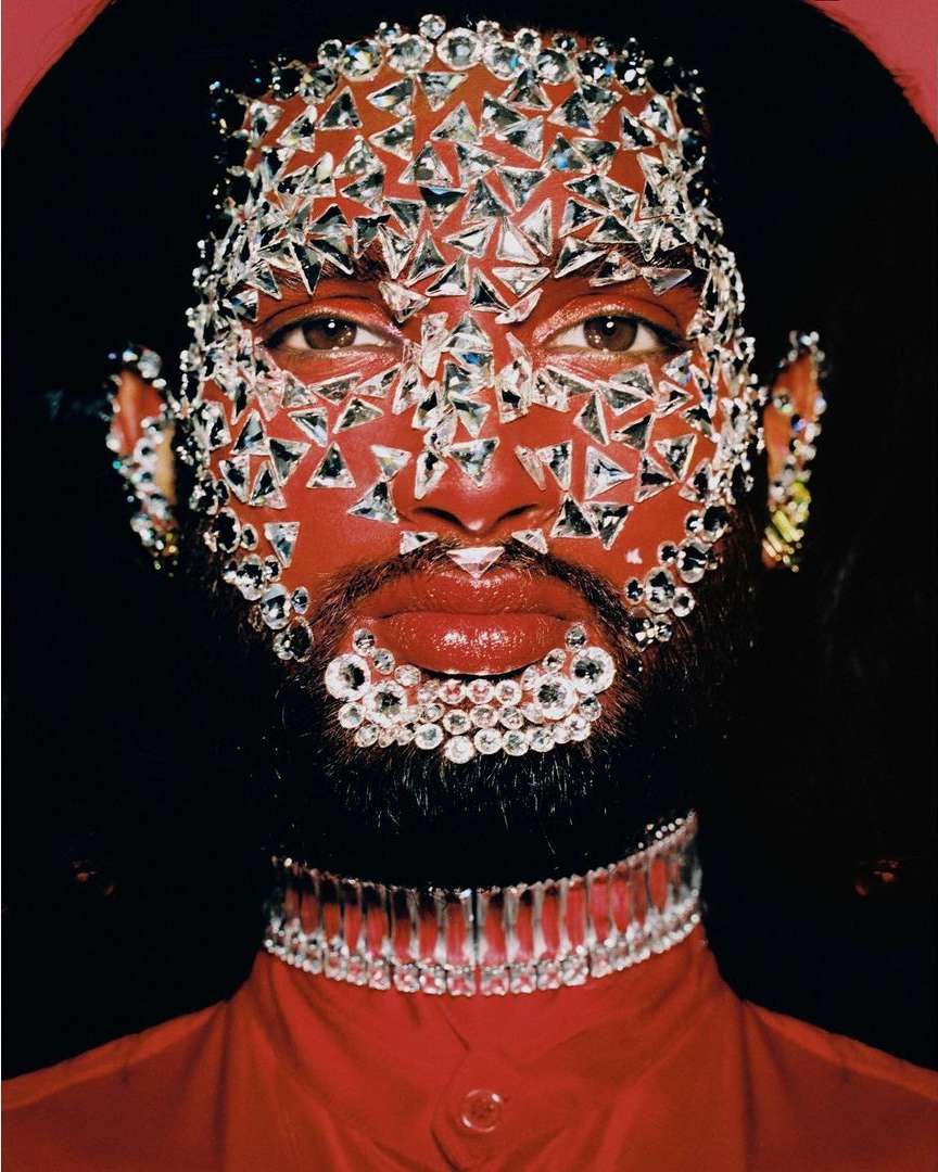 Artistic close-up studio portrait of a person with vibrant red skin, adorned in rhinestones, and wearing a red top and rhinestone choker.