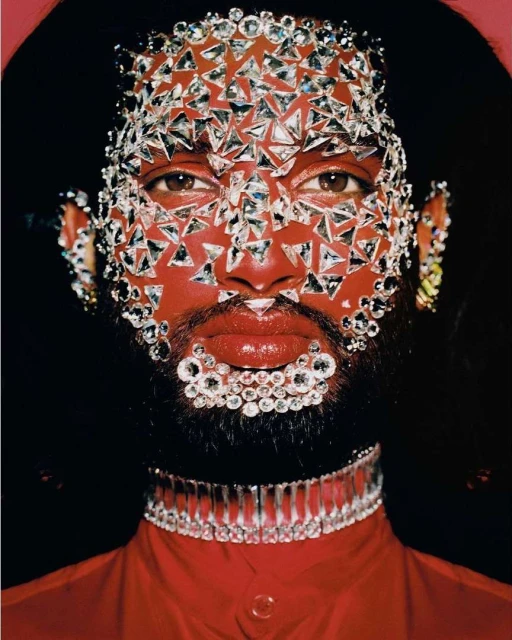 Artistic close-up studio portrait of a person with vibrant red skin, adorned in rhinestones, and wearing a red top and rhinestone choker.
