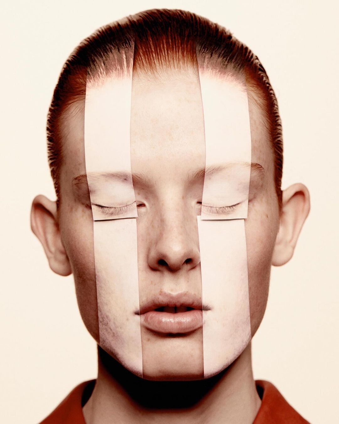 Close-up studio shot of a young adult woman with red hair and pale skin with paper strips obscuring parts of her face.