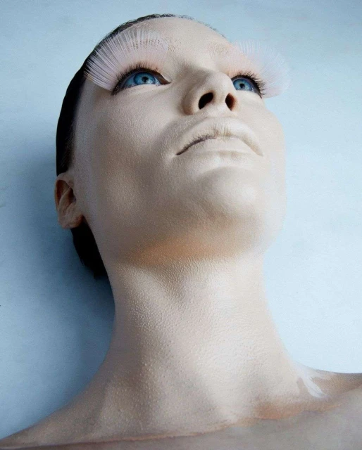 Woman with face paint and feather eyelashes looking up. Beauty shot, head and shoulders. Light blue background, close-up, portrait.