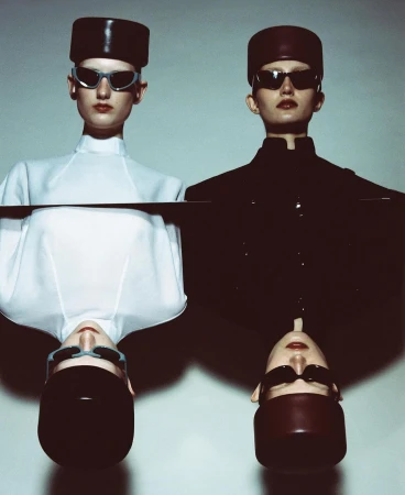 Two models wearing structured hats and sunglasses, one in white and one in black, in a mirrored vertical composition by Carlijn Jacobs
