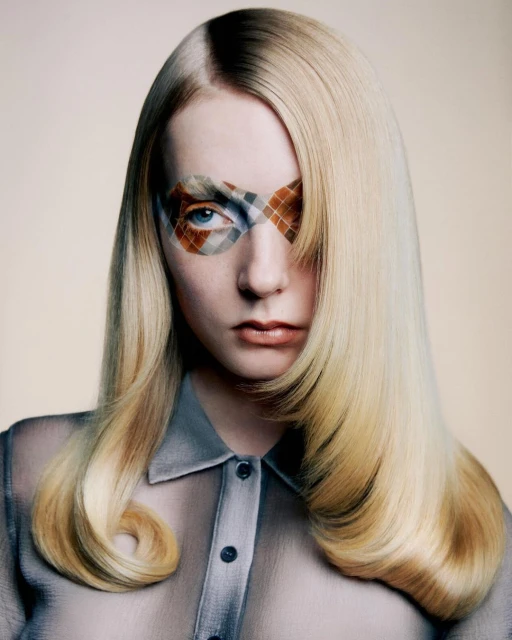 Close-up studio shot of a blonde woman with light skin, posing and looking directly at the camera, wearing a sheer button-down shirt.