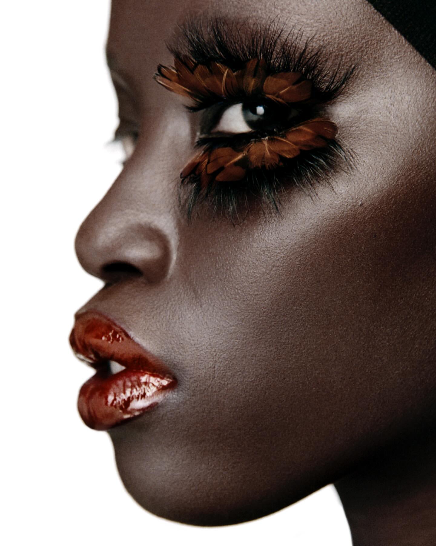 Profile of a Black woman's face with long, feathered eyelashes, wearing red lipstick, and a black head covering on a white backdrop.