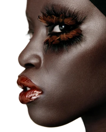Profile of a Black woman's face with long, feathered eyelashes, wearing red lipstick, and a black head covering on a white backdrop.