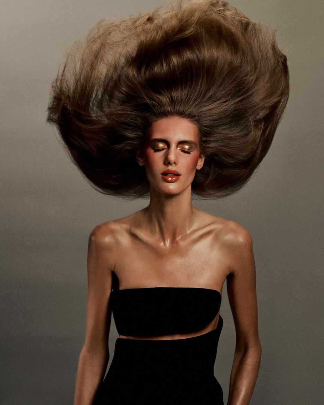 Fashion shot of a woman with dramatic blonde hair, wearing a black strapless top with open midriff, and glossy makeup. Beauty advertisement.