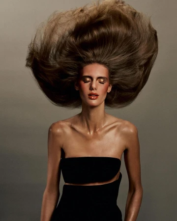 Fashion shot of a woman with dramatic blonde hair, wearing a black strapless top with open midriff, and glossy makeup. Beauty advertisement.