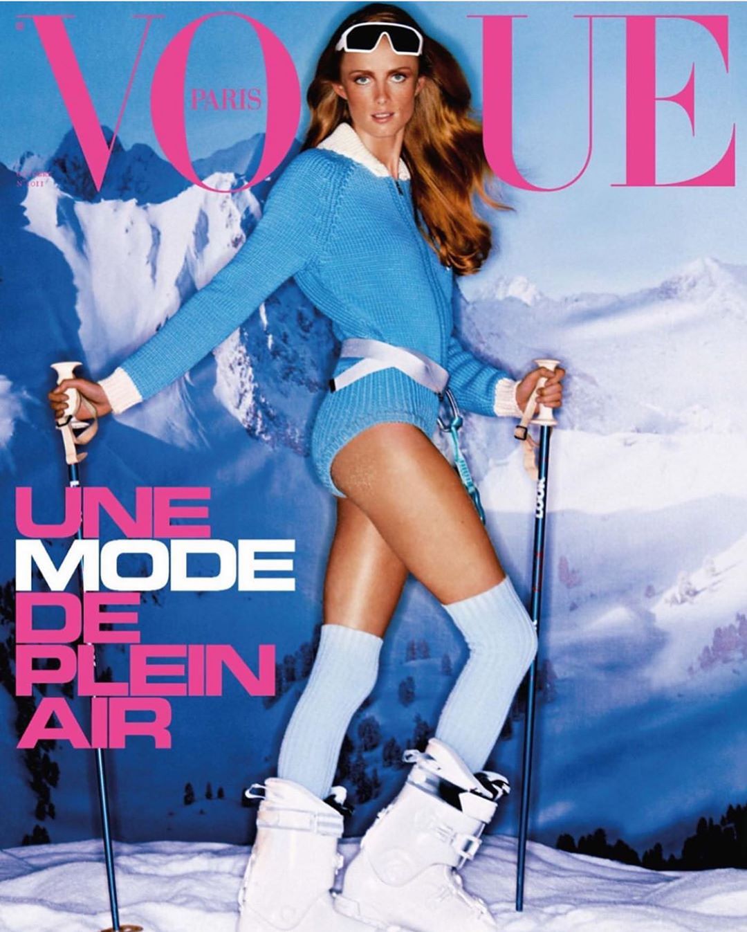 Fashion editorial cover featuring a female model in blue ski suit with ski poles and boots, posing in front of snowy mountains.
